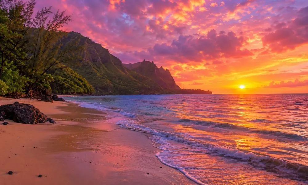 A breathtaking pink and gold watercolour sunset over Ke'e Beach on Kauai, Hawaii, with lush green cliffs, white sand, and vivid blue water at the start of the Kalalau Trail